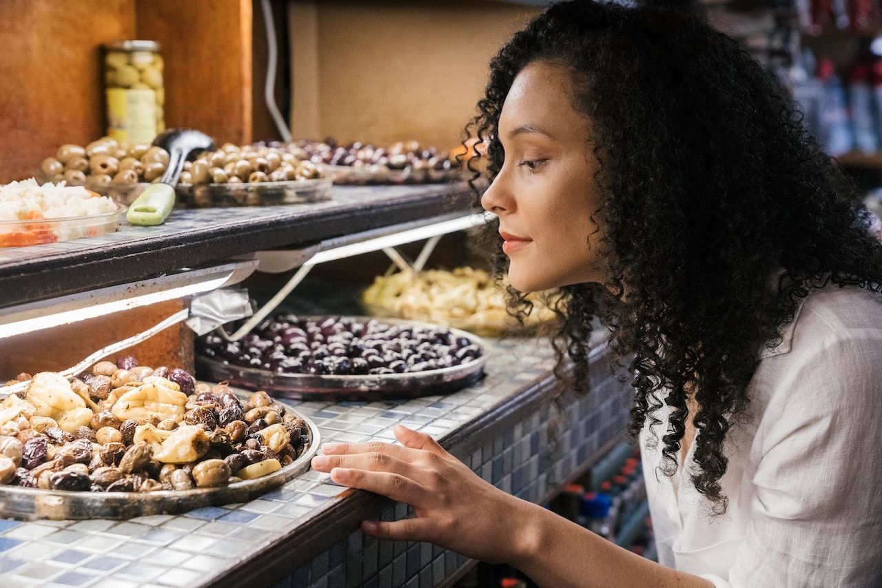 woman with curly hair looking at an olive bar buffet