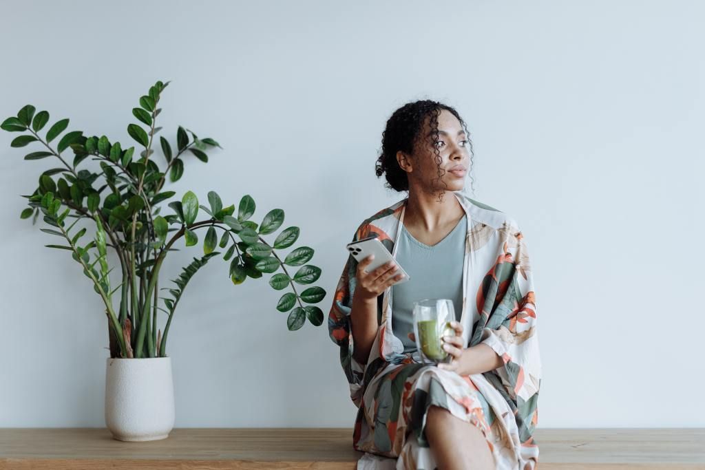 Black woman sitting on counter drinking green juice wondering how to stay safe from surrogacy scams